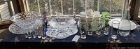 Wide view of all lot items displayed on table under window. Includes punch bowl, decanters, glasses, cups and vases.