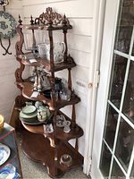 Five-level tiered wooden shelf with shelves filled with various glassware and dishes, not included in sale.
