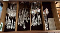 Photo of silver plate forks, spoons and serving pieces with ornate handles organized in wooden drawer