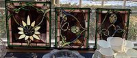 Three stained glass panels side by side on a window sill, showing overall size and design variation