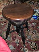 Side view of vintage piano stool showing turned legs and glass ball claw feet on a patterned rug.