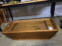 Side view of the wooden doughbox showing rectangular shape, flat lid, open handles, and patina.