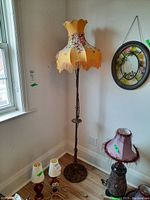 Full view of the antique floor lamp near window showing its tall metal base and scalloped floral fabric shade with fringe.