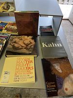 Photo showing a Lucian Freud art book with a reclining nude figure on the cover, a large Kahn architecture book, a black and red Anish Kapoor book, and a yellow Seven Master Print-Makers catalog from MoMA.