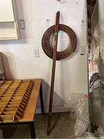 Photo showing six straight copper pipes, approx. 0.5 inch diameter, leaning against a white wall with a coiled copper tubing reel behind them.