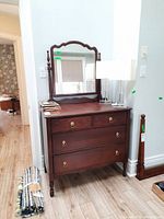 Photo showing solid wood dresser with four drawers and framed mirror mounted on top, minor wear visible on the wood surface.