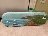Full view of the painted driftwood artwork showing the coastal village scene with boats and buildings.