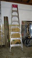 Front view of aluminum step ladder standing upright against wall in garage setting, showing red top tray and 8 steps.
