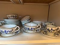 Multiple tea cups and saucers arranged on shelf with matching pattern visible