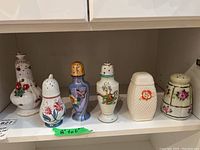 Six antique and vintage sugar shakers in various shapes and designs with floral motifs and different colors.