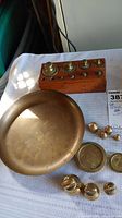 View of brass balance pan, wooden holder with small brass weights, and assorted loose weights on table