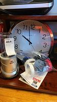 Photo showing the Big Boss blender/mixer base in silver, a transparent container, multiple attachments in plastic bags, an instruction manual, and a large wall clock in the background.