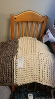 Knitted wool blanket draped on a wooden chair showing cream and brown sections with visible knit texture.
