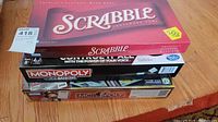 Stack of board games including Scrabble on top and two electronic Monopoly games below.