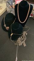 Photo of multiple costume jewellery necklaces on black display busts showing variety of chain styles and centerpiece pendants