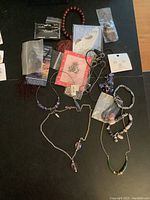 Photo showing various bracelets, earrings, necklaces, prayer beads, pin and keychain laid out on a dark surface.