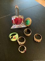 Photo displaying six costume rings arranged with the clear acrylic ring holder containing red decorative elements on a black surface.