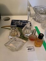 Top-down photo showing 3 vintage glass perfume bottles with faceted stoppers, 2 small perfume bottles, a blue box, and a clear cut-glass trinket box, with a green decorative piece.