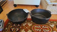 Two cast iron pots displayed side by side on a patterned rug with wooden floor in the background.