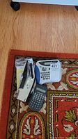 Photo of two label makers and one calculator on a wood floor and patterned carpet.