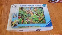 Photo showing two Ravensburger puzzles stacked, 300 piece puzzle box visible with colorful jungle and animal artwork.