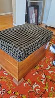 Side angle view of a wooden record storage bench with a tufted cushioned seat covered in black and white houndstooth fabric. The bench sits on a patterned orange rug.
