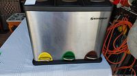 Front view of a stainless steel kitchen recycle bin with three foot pedals in yellow, green, and brown.