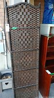 Front view of the dark brown woven rattan tri-fold screen showing the lattice weave pattern and rounded top edges.