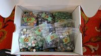 Top view of white box containing several clear plastic bags of marbles, each bag labeled with quantities such as 50, 40, and 30 marbles.