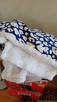 Close-up of blue fleece snuggie with white abstract pattern and thick white sherpa lining, folded on a surface.