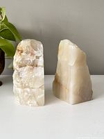 Front view showing two alabaster bookends standing upright, one with rougher crystal texture and colored veining, the other smoother with light brown lines.