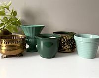 Front view of five vintage plant cover pots, including brass and pottery types in various green shades and brass with patina.