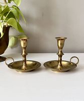 Two brass chamber candlestick holders side by side, showing full items with handles and drip plates.