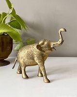 Side view of brass elephant figurine showing engraved floral pattern and raised trunk.