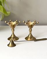 Front view of two brass jester top candlestick holders and accompanying candle snuffer on table