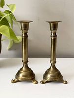 Front view of two vintage brass candlestick holders with three curled legs and cylindrical stems.