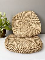 Pair of vintage large coiled wicker seating cushions stacked, showing spiral coil texture and beige color.