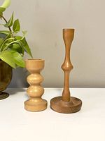 Front view of the pair of wooden candlestick holders placed on a white surface with a plant in the background.