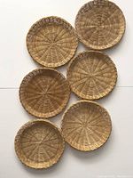 Six vintage wicker charger plates arranged flat, showing the top woven pattern and shallow rim. Natural brown color and consistent size about 9 inches across.
