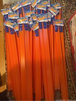 All twenty 24-inch orange straight Hot Wheels track pieces with original packaging tags neatly laid out to show quantity and condition.
