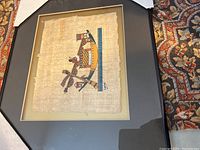 Full view of framed hand-painted Egyptian papyrus showing figure with traditional patterns.