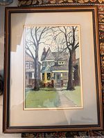 Full-frontal photo of watercolor painting depicting a two-story house with large trees, framed and matted.