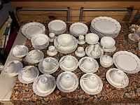 Full layout of the dinnerware set showing plates, bowls, cups, and saucers with floral pattern on a patterned tablecloth.