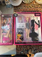 Two boxed Barbie dolls side by side on floral carpet - 1959 50th anniversary Barbie larger boxed doll and 2009 Barbie in pink and black swimsuit smaller boxed doll