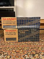Stacked original boxes for Sharp SA-X25C receiver and RT-W6000 cassette deck on a patterned carpet.