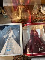 Photo of all three Barbie dolls in their boxes: 50th Anniversary Barbie in gold gown, Holiday Visions Barbie in white gown with damaged box, and Holiday Celebration Barbie in burgundy gown.
