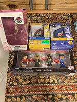 Boxed Gallery Figures Mew Psychic figure, Pixel Pals Mario and Batman boxed figures, and Tube Heroes 4-pack boxed figures on carpeted floor with wooden wall background.