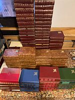 Wide view of stacks of hardcover Reader's Digest books in various colors and bindings, arranged neatly in rows and columns on a patterned rug and surface, some in slipcases.