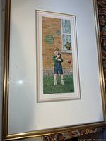 Full view of the framed art print showing the boy holding a black kitten with a brick wall background and flower pot in the window