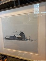 Framed artwork showing the winter barn scene with snow and signature label below the image.